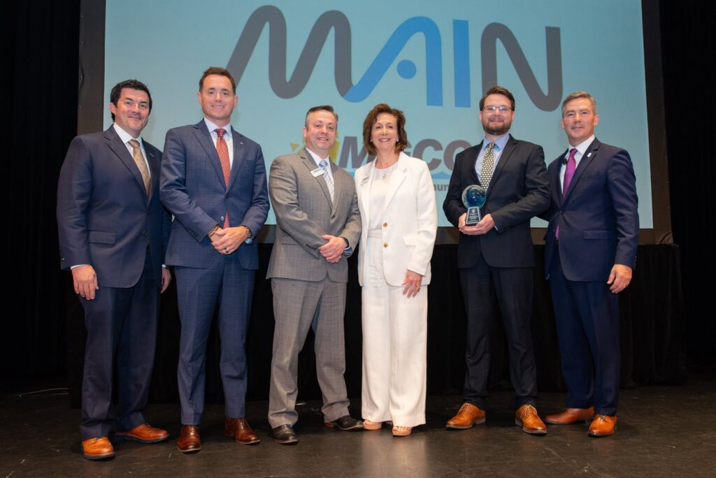 Six people pose onstage as a MAIN representative holds the 2026 Rising Tide Award at the State of the Coast Symposium.