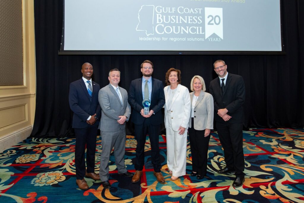Six people pose with the 2026 Rising Tide Award beneath the Gulf Coast Business Council’s 20th-anniversary screen.