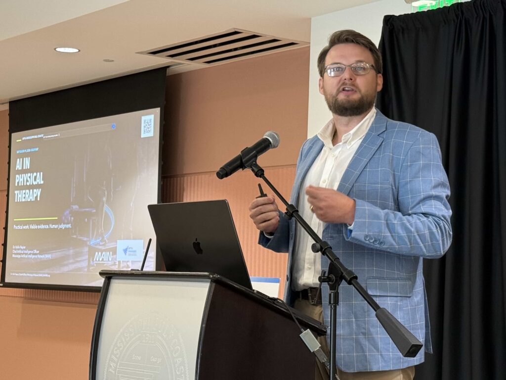 Dr. Kollin Napier speaks beside a projected AI in Physical Therapy presentation slide.