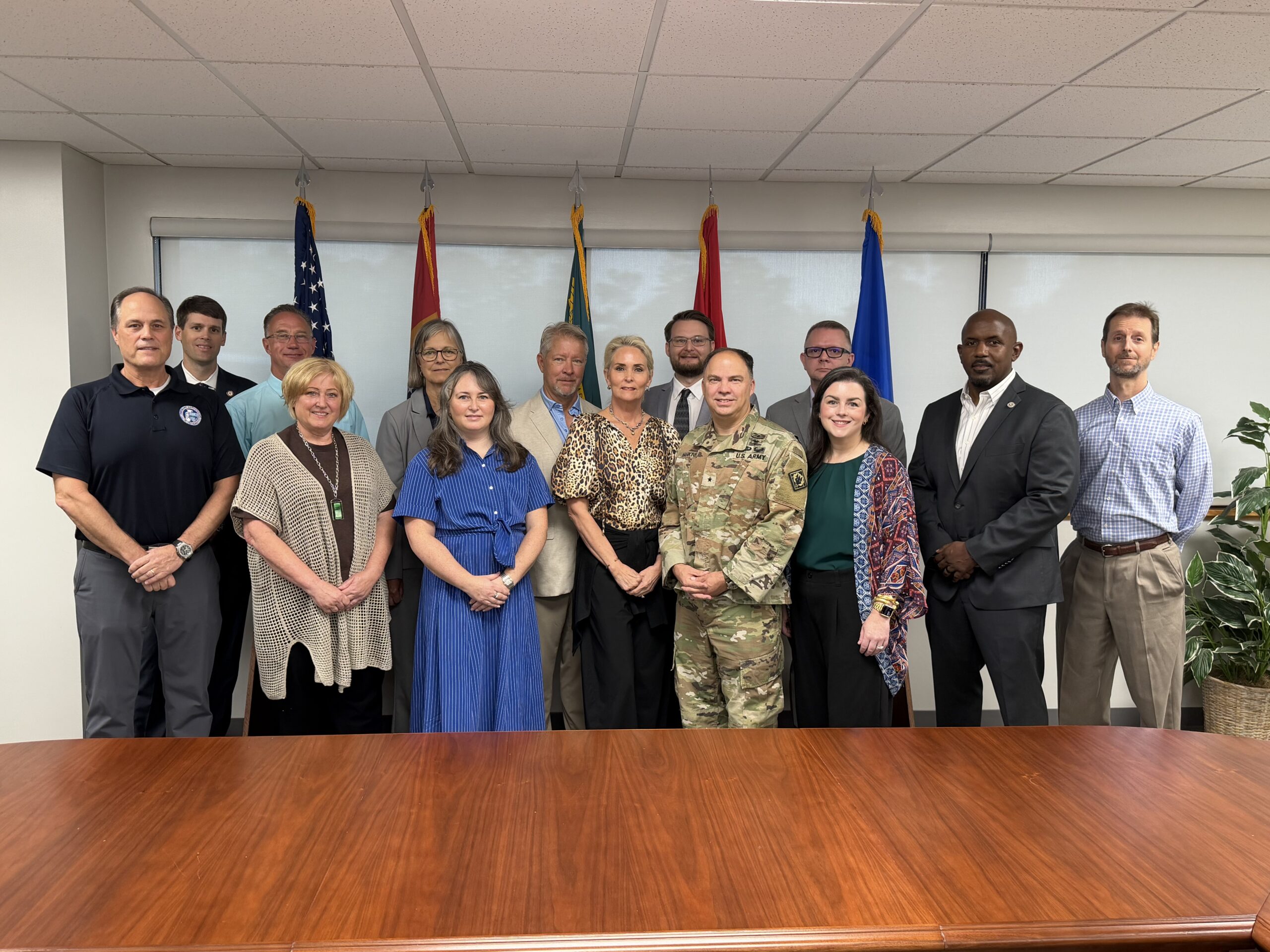 Task force members and invited speakers stand together in a meeting room at Camp Shelby.