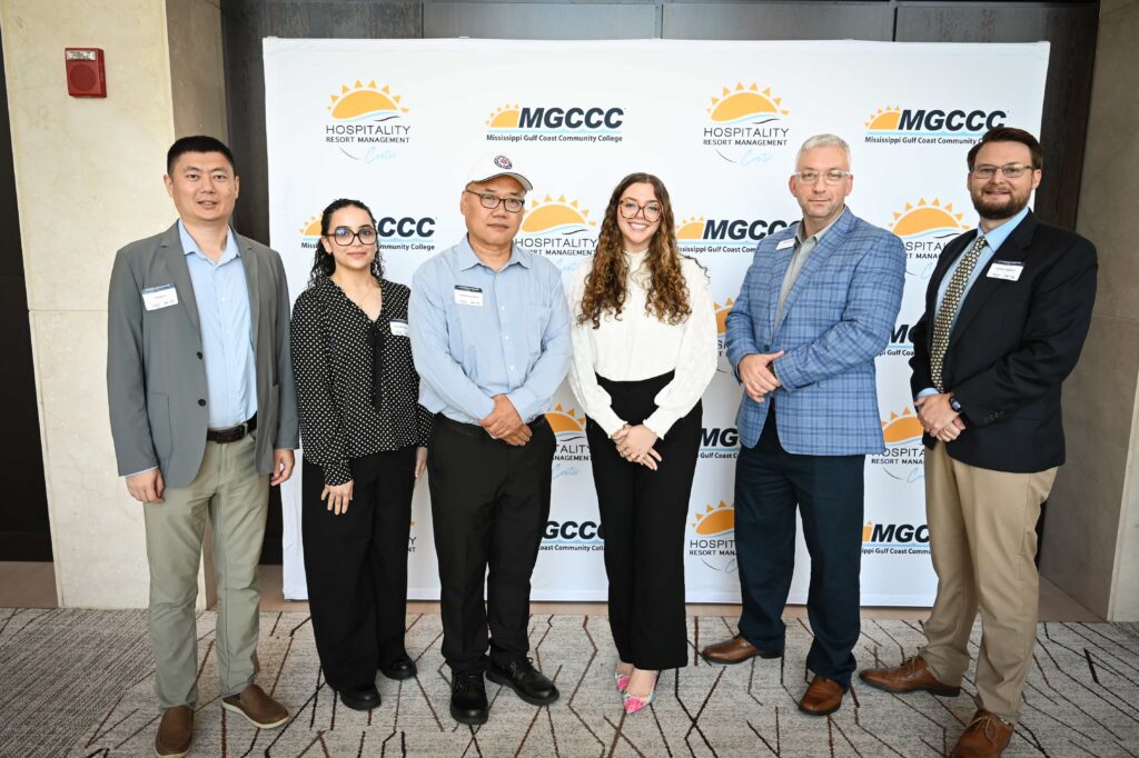 Six AI in Manufacturing Day researchers and hosts stand in front of an MGCCC Hospitality & Resort Management backdrop.
