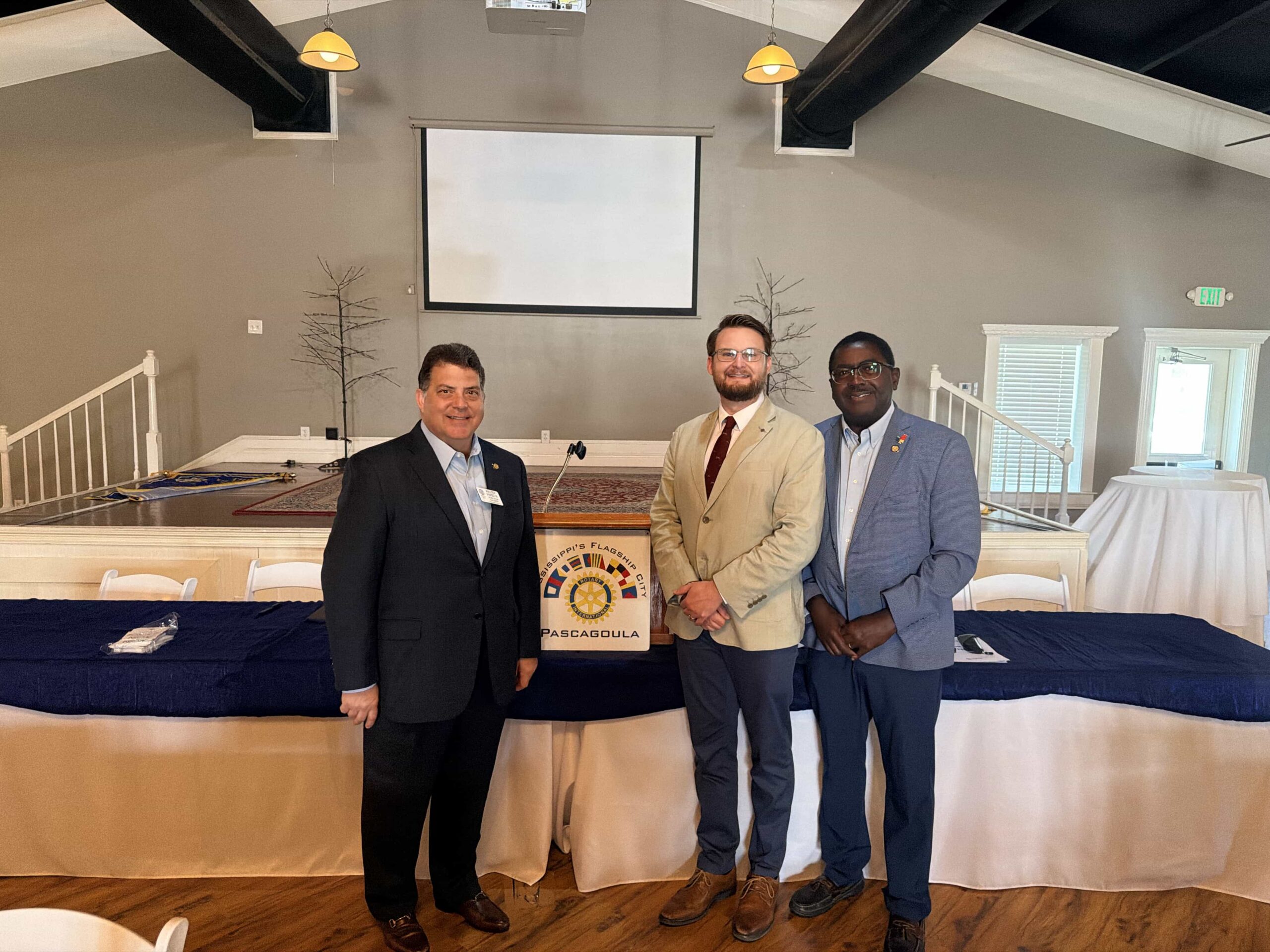 Dr. Kollin Napier stands between two attendees in front of a Pascagoula Rotary podium.