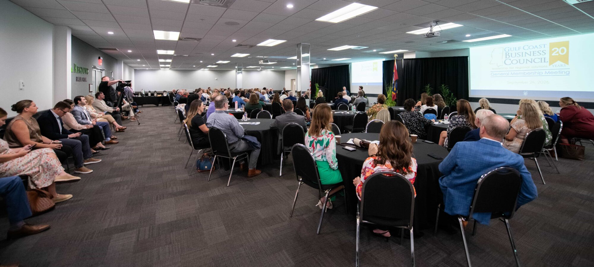 Audience at the Gulf Coast Business Council meeting, with Jamie Miller and Dr. Kollin Napier speaking onstage.