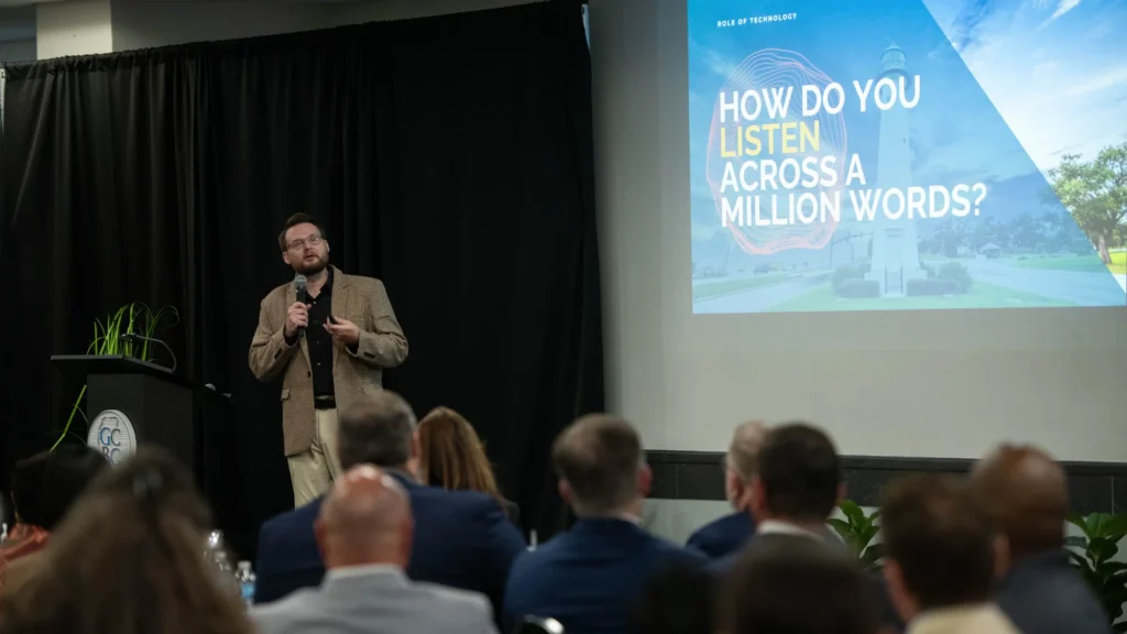 Dr. Kollin Napier presents beside a slide asking how to listen across a million words, with class presentation attendees in the foreground.